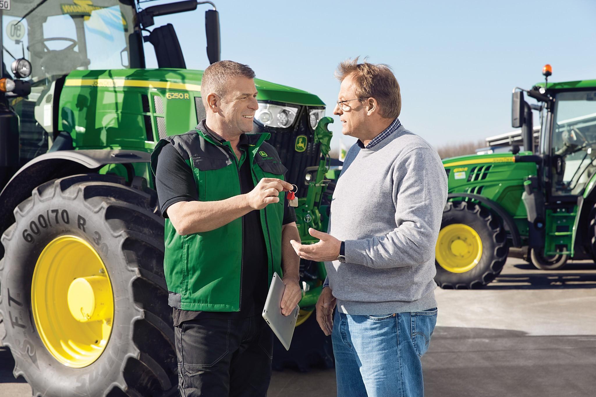 Verkoper overhandigt de sleutels van een nieuwe John Deere 6250R-tractor aan een klant