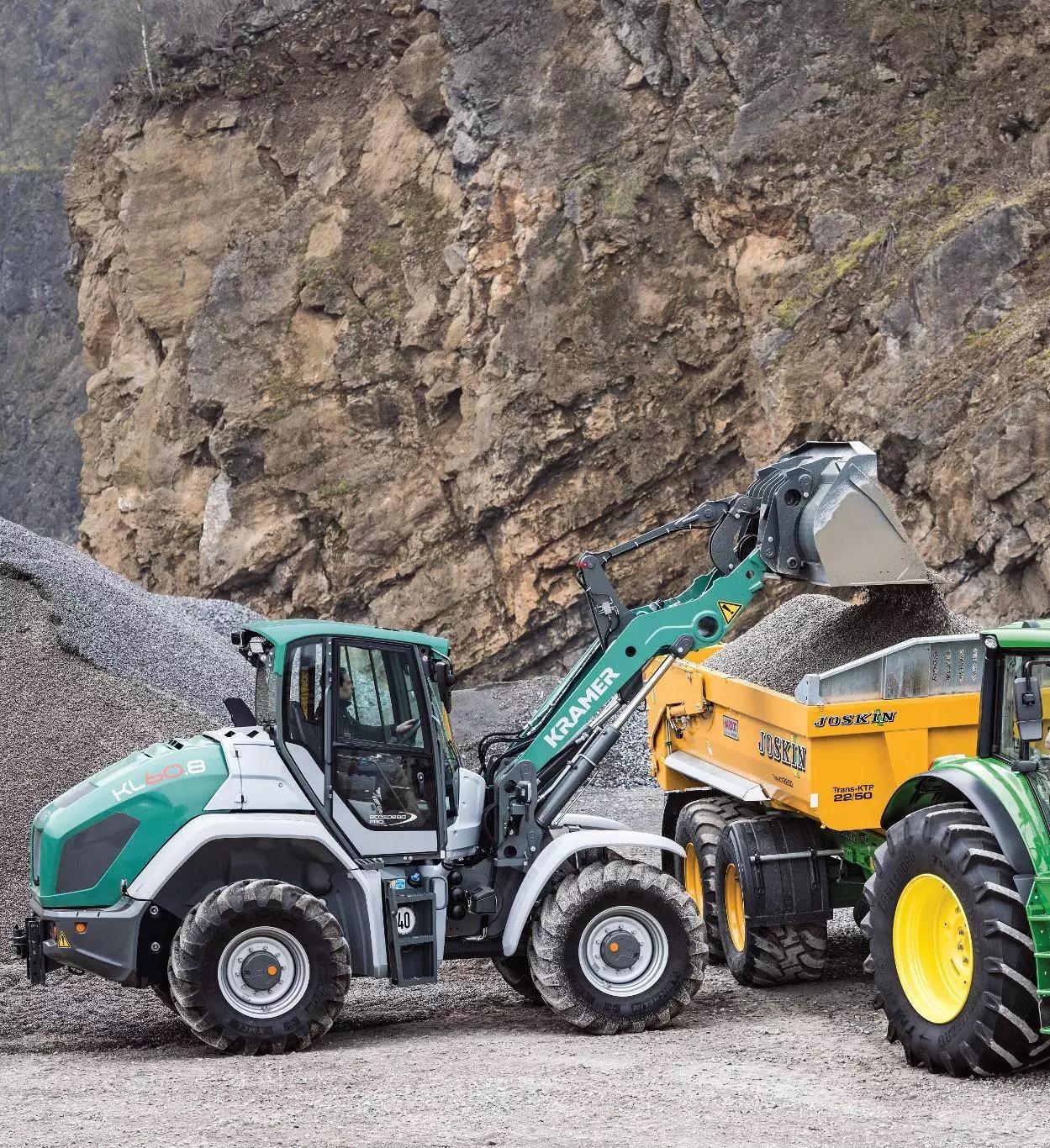 Kramer KL60.8 wiellader laadt grind in een Joskin kipwagen achter een John Deere-tractor