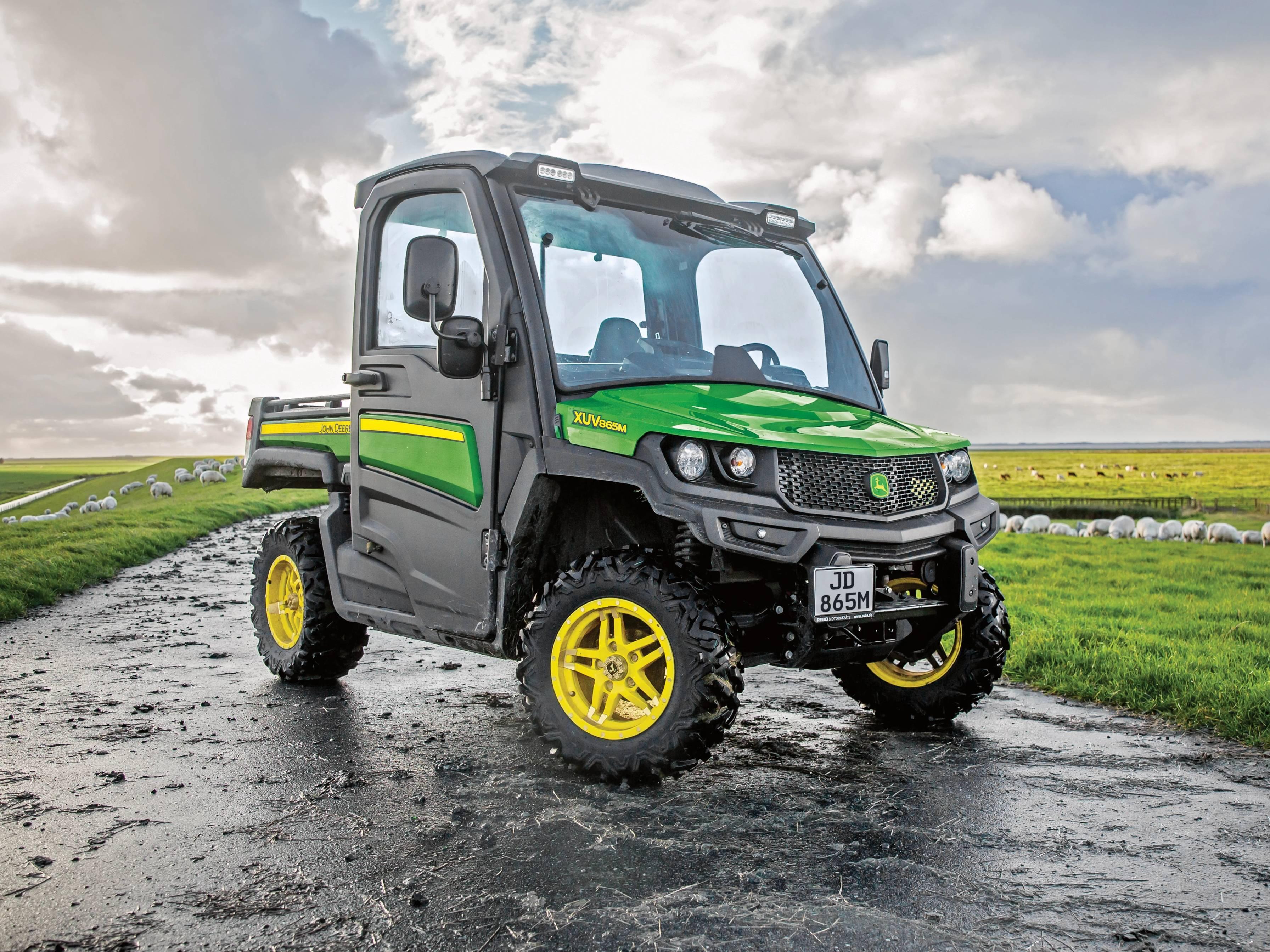 John Deere Gator XUV865M terreinvoertuig met cabine op een landweg tussen de weilanden
